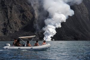 Des gens observent la lave plonger dans la mer depuis leur bateau.